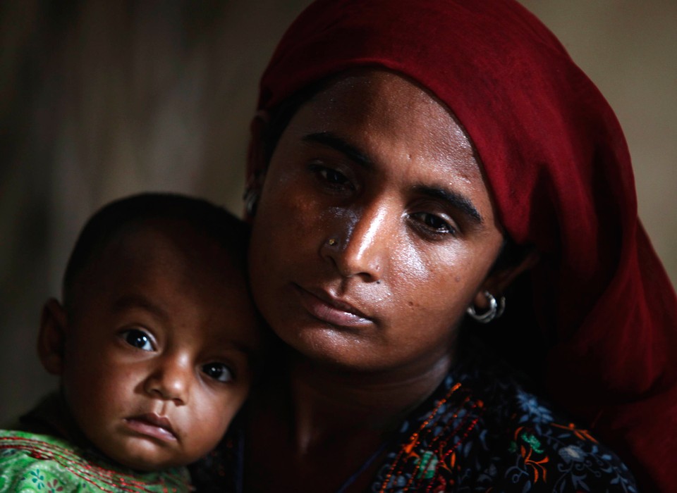 A woman and her baby wait for food handouts with other flood victims as they take refuge at a make-shift camp in Sukkur