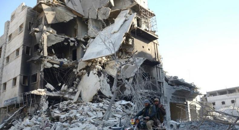 Rebels ride a motorcycle past a destroyed building in the northwestern Syrian border town of al-Bab on February 25, 2017