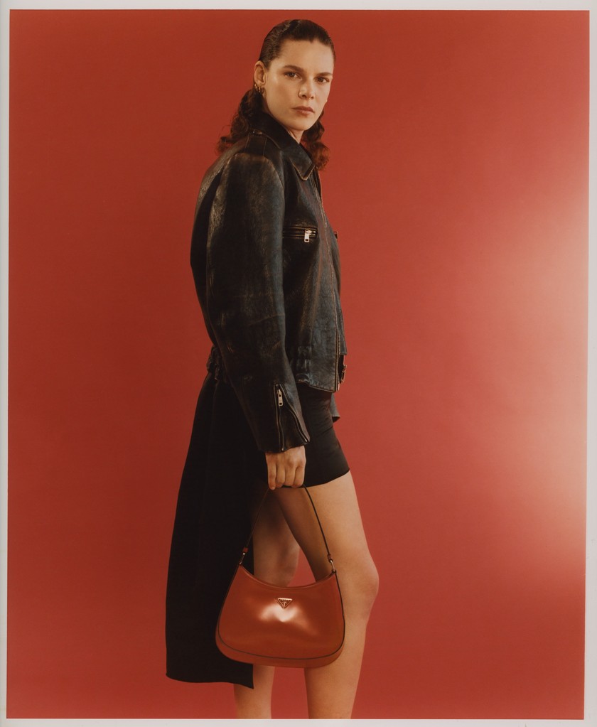 Oversize-Bikerjacke in Used-Optik, Minirock aus Doppelsati, mit abnehmbarer Schleppe und Schultertasche Cleo aus gebürstetem Leder, alles von Prada.