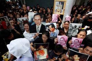 People hold portraits of Thailand's late King Bhumibol Adulyadejas as they wait on the roadside whil