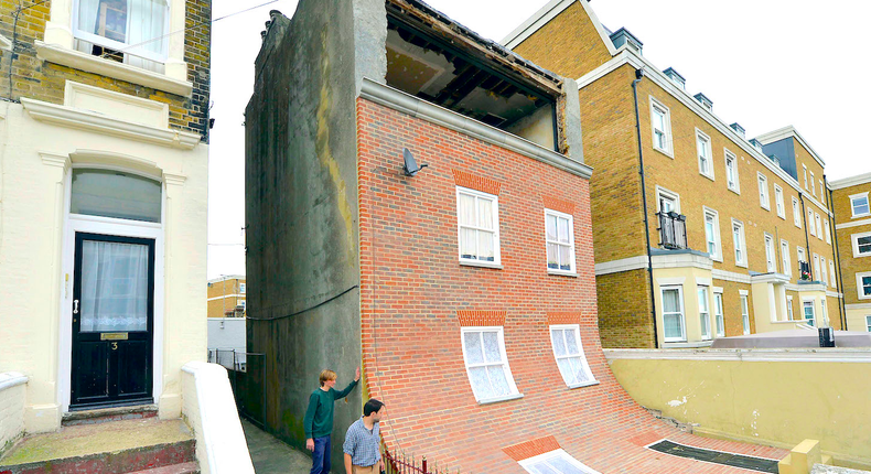 Passers-by look at a piece of public art, depicting a sliding house in a residential road in Margate, southern England October 9, 2013.