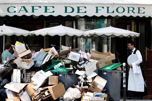 A waiter stands near a pile of rubbish bags in front of the Cafe de Flore in Paris during a strike of garbage collectors and sewer workers of the city of Paris to protest the labour reforms law proposal