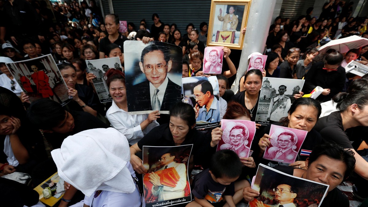 People hold portraits of Thailand's late King Bhumibol Adulyadejas as they wait on the roadside whil