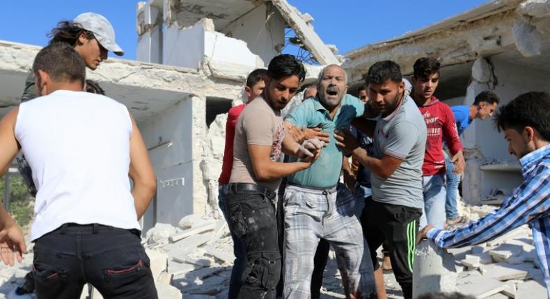 Syrian civilians help a wounded man following reported air strikes by regime forces on Maaret al-Numan in Syria's northwestern Idlib province on July 23, 2019