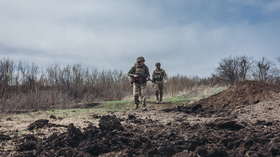 Ukraińscy żołnierze przechodzą obok dziury po pocisku na ukraińskiej linii frontu w Donbasie