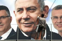 A labourer works on hanging up a Likud election campaign banner depicting Israeli Prime Minister Ben