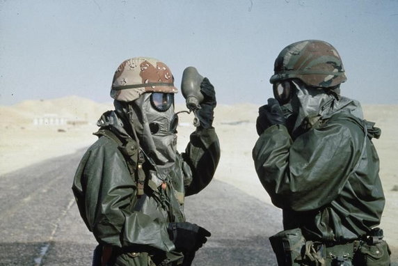 Dwaj żołnierze w uniformach chroniących m.in. przed atakiem chemicznym. Żołnierz po lewej pije wodę z menażki bez zdejmowania maski (domena publiczna).