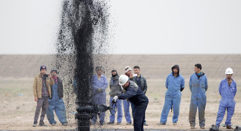 Iraqi workers stand near a pipeline as it ejects oil at Al Tuba oil field in Basra, southeast of Baghdad