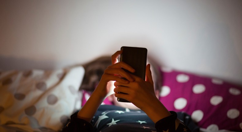 Girl lying on bed at night and using a mobile phone