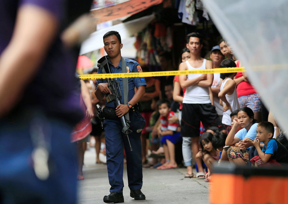 A member of the Philippine National Police (PNP) stands guard while residents look on near the scene where two suspected drug pushers were killed during a police operation, in metro Manila.