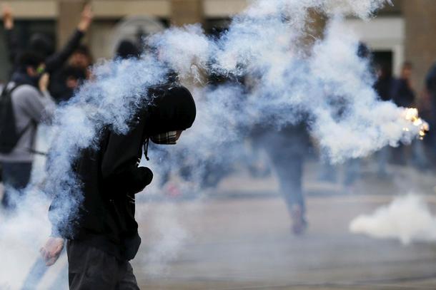 Youth takes cover from tear gas grenades during a demonstration against the French labour law propos