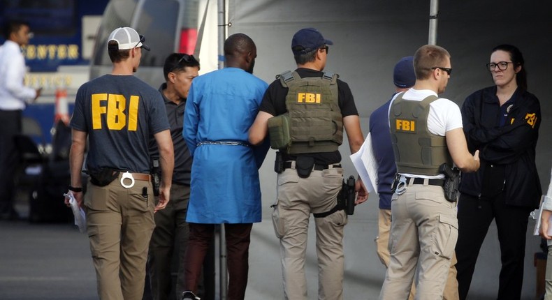 Federal agents hold a cyberfraud suspect, second from left, at a downtown Los Angeles parking lot after predawn raids that saw dozens of people arrested in the L.A. area on Thursday, Aug. 22, 2019 [AP Photo/Reed Saxon]