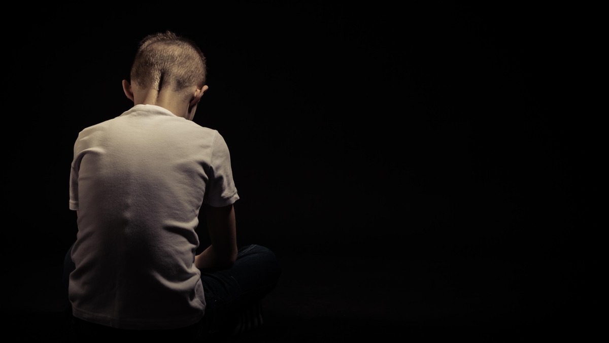 Rear View of a Seated Sad Young Boy Against Black