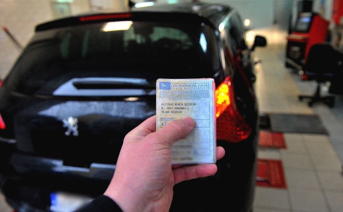 Zbliżenie na rękę trzymającą dowód rejestracyjny pojazdu, w tle samochód osobowy podczas badania technicznego