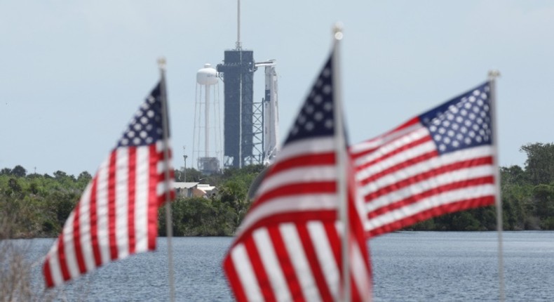 A SpaceX Falcon 9 rocket with the Crew Dragon spacecraft looms in the distance at launch complex 39A as American flags flutter in the wind, at the Kennedy Space Center in Florida on May 29