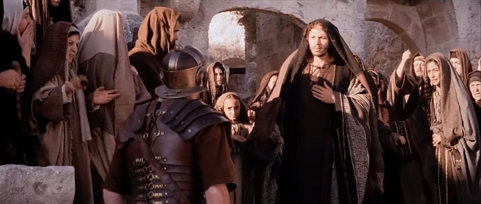 Żołnierz rozkazuje Szymonowi pomóc dźwigać krzyż Jezusa | Kadr z filmu "Pasja' Mela Gibsona