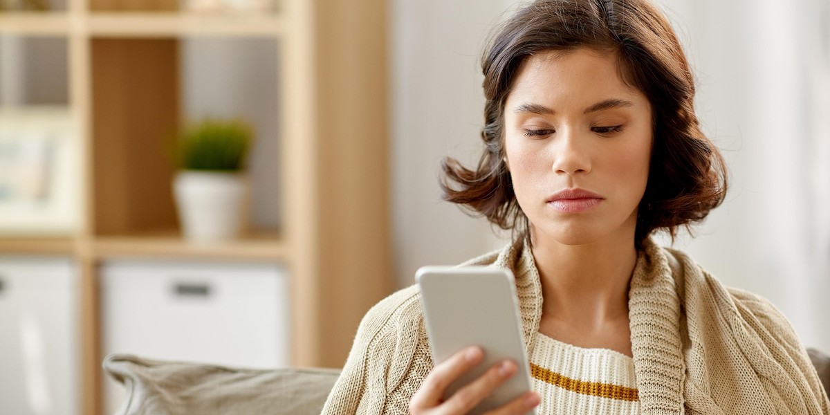 sad woman in blanket using smartphone at home