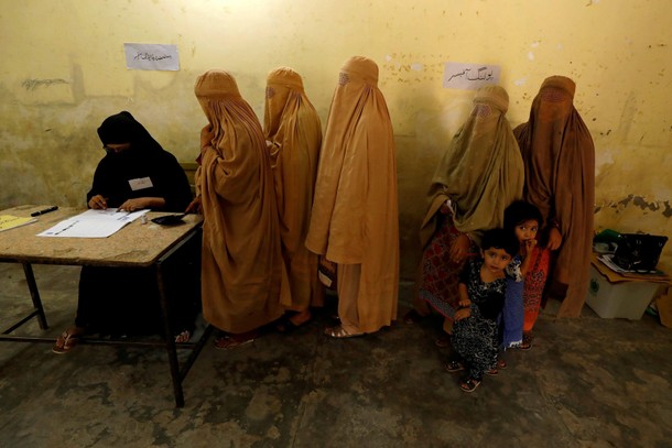 Women, clad in burqas, stand in line to cast their ballot at a polling station during general electi