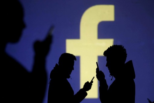 FILE PHOTO: Silhouettes of mobile users are seen next to a screen projection of Facebook logo in thi