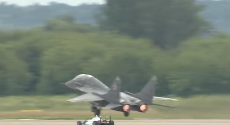 A Formula One car racing a MiG-29 fighter jet.