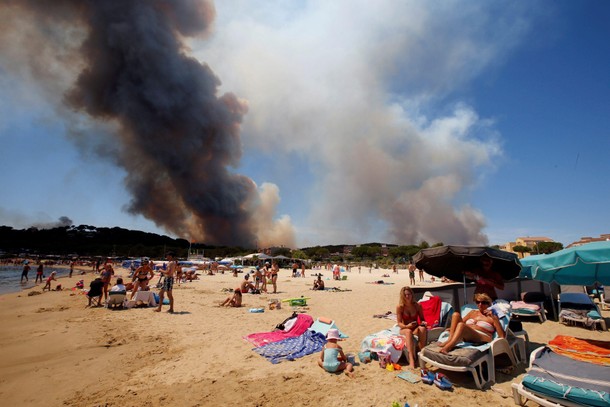 Smoke fills the sky above a burning hillside as tourists relax on the beach in Bormes-les-Mimosas