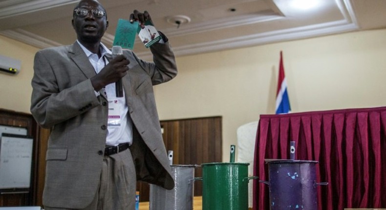 An IEC (Independent Electoral Commission) official shows an electoral document of incumbent president Yahya Jammeh next to the ballot boxes with the three parties colours on November 28, 2016