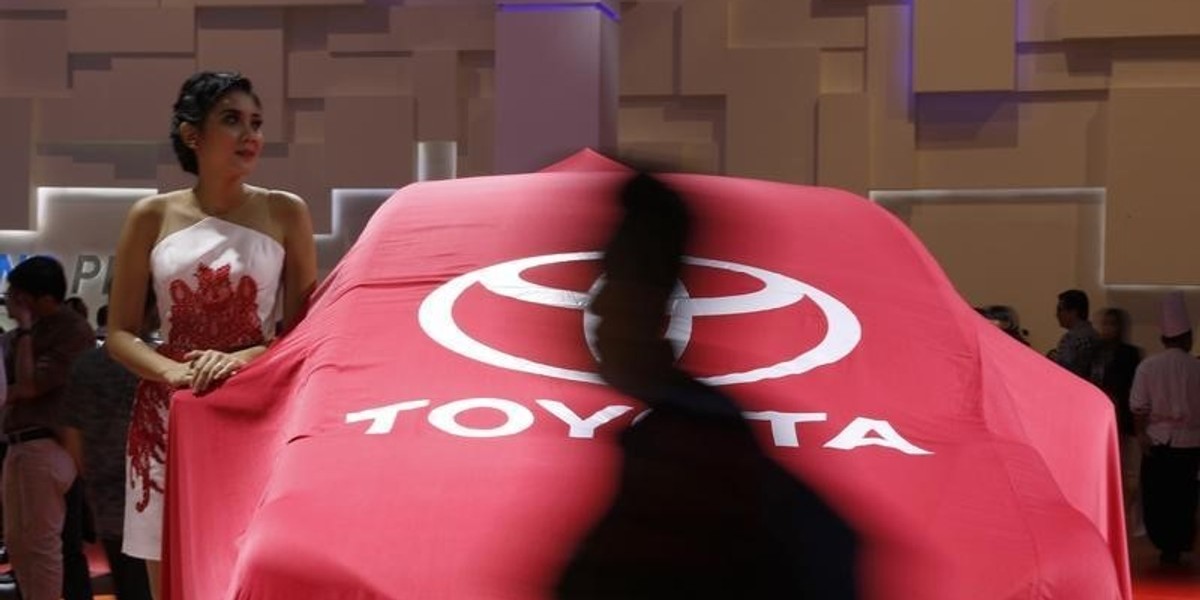 A model stands beside a veiled, new Toyota Sienta car at the Indonesian International Motor Show in Jakarta