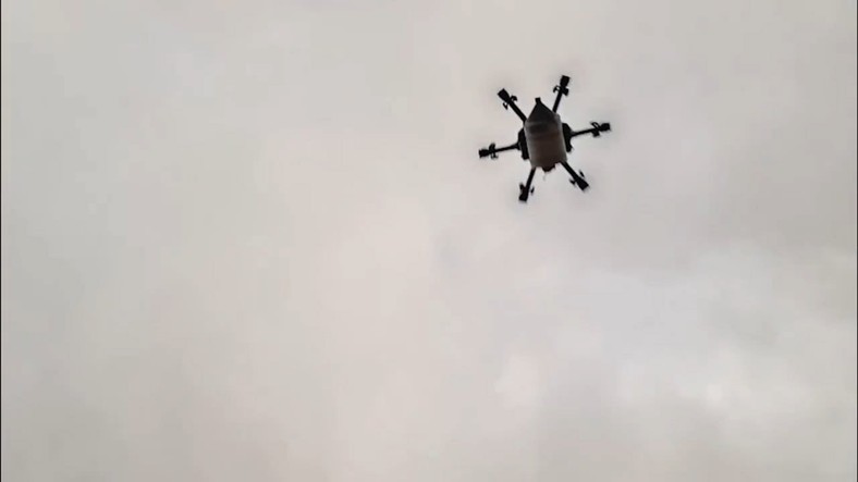 Na zdjęciu widać kształt dronu i podwieszoną pod nim szpulę ze światłowodem