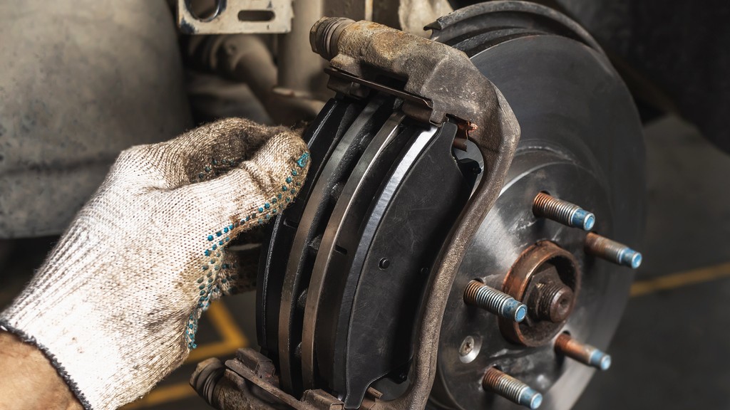 Detailný záber na brzdový strmeň a hadičku, kde mechanik hľadá stopy úniku brzdovej kvapaliny.  