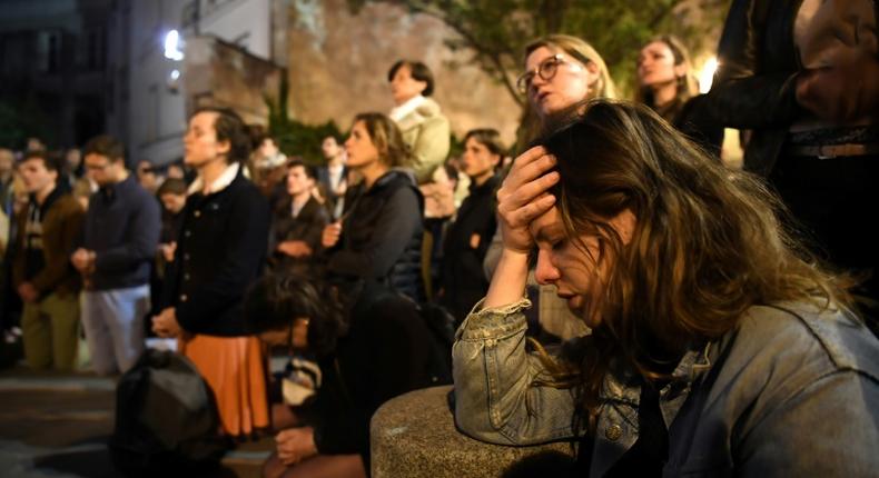 Onlookers react as they watch flames engulf Notre-Dame Cathedral in Paris on April 15, 2019