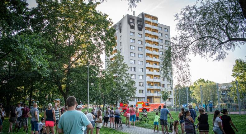 People look on as firefighters work at the scene where a fire broke out in an apartment block in Bohumin, eastern Czech Republic on August 8, 2020, killing eleven people including three children