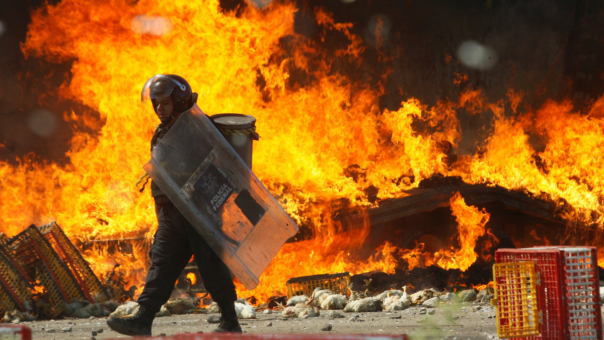 A riot police officer walks past a burned truck carrying chickens after clash with protesters from the National Coordination of Education Workers (CNTE) teachers’ union during a protest, in Nochixtlan