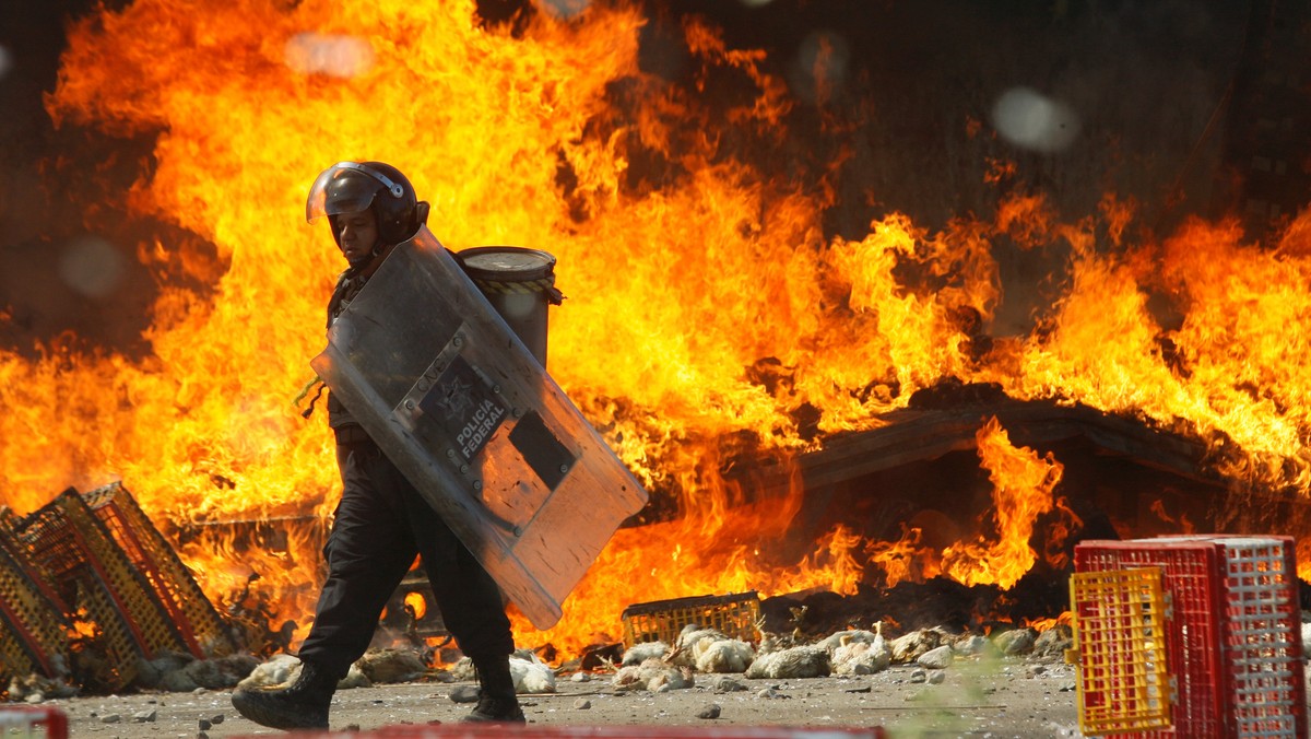 A riot police officer walks past a burned truck carrying chickens after clash with protesters from the National Coordination of Education Workers (CNTE) teachers’ union during a protest, in Nochixtlan