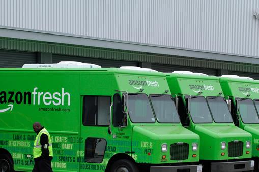 A worker walks past Amazon Fresh delivery vans parked at an Amazon Fresh warehouse in Inglewood