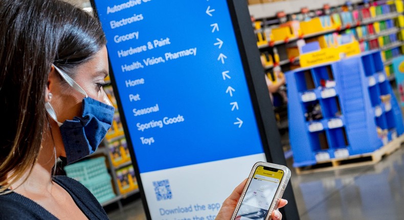 A Walmart shopper checks the company's mobile app next to a store directory.