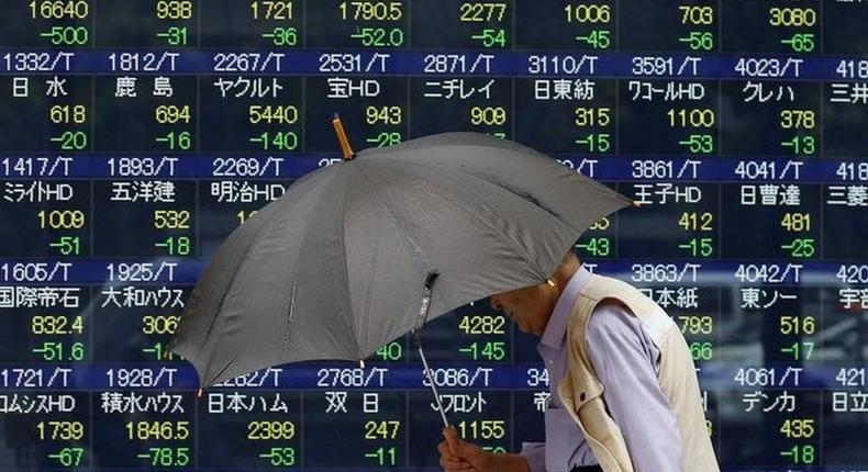 A pedestrian holding an umbrella walks past a stock quotation board outside a brokerage in Tokyo, Japan, June 13, 2016. 