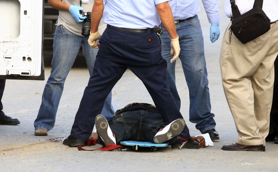 Forensic workers stand over the headless body of a man in Tijuana, October 12, 2010.
