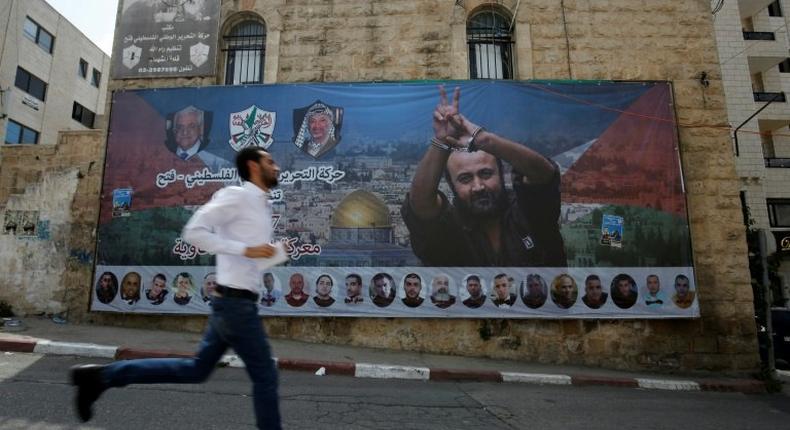 File picture of a man running past a poster of Palestinian hunger-striker and prominent prisoner Marwan Barghouti in the West Bank city of Ramallah on May 3, 2017