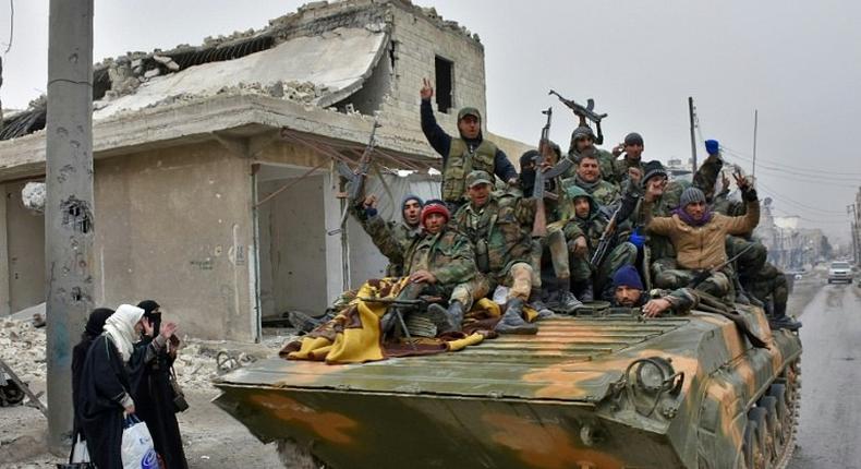 Syrian pro-government forces cheer on a military vehicle driving past residents on November 30, 2016 fleeing a former rebel-held district of eastern Aleppo, northern Syria which was retaken by the regime forces last week