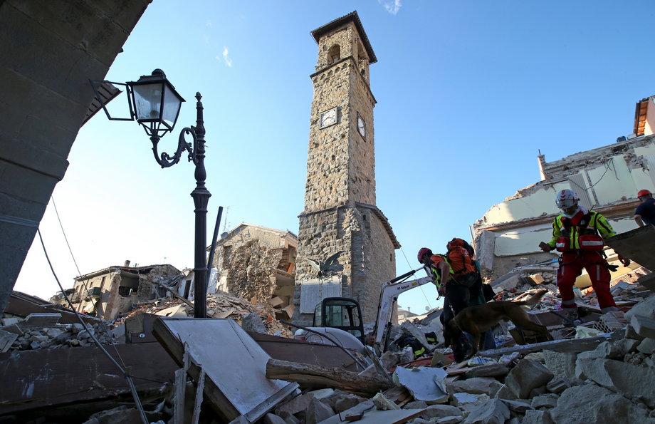 Rescuers walk past the tower with the clock showing the time of the earthquake on August 24.