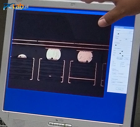 ...i mikroskopowej (fałszywe kolory). Na obrazie widać warstwy miedzi w płytce drukowanej GPU (dwie linie na górze), kulki spoiwa lutowniczego (jasne koła), strukturę laminatu płytki drukowanej (nieregularne, przemienne jasne i ciemne pasy na dole) i przelotki łączące obie strony laminatu (jedna przelotka przypomina parę nawiasów kwadratowych)