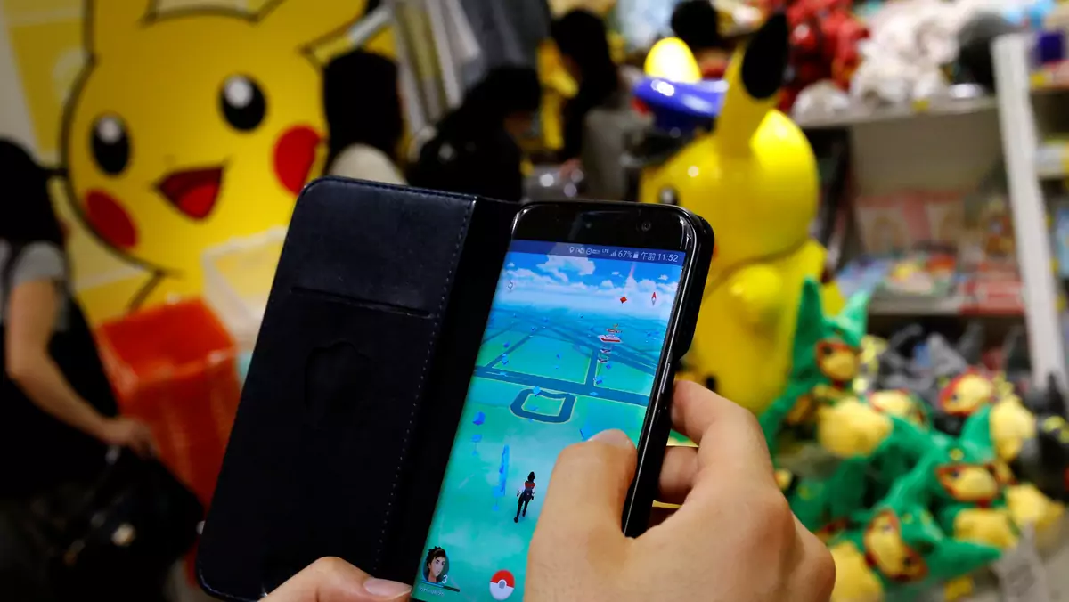 A man plays the augmented reality mobile game "Pokemon Go" by Nintendo in front of a shop selling Pokemon goods in Tokyo