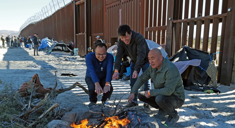 Chinese Migrants attempting to cross into the US from Mexico sit by a fire as they are detained by US Customs and Border Protection at the border on November 12, 2023, in Jacumba, California.Nick Ut/Getty Images