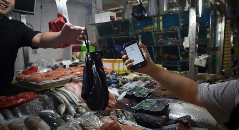 This photo taken on June 27, 2017 shows a man making purchases through his smartphone at a seafood booth at a market in Beijing