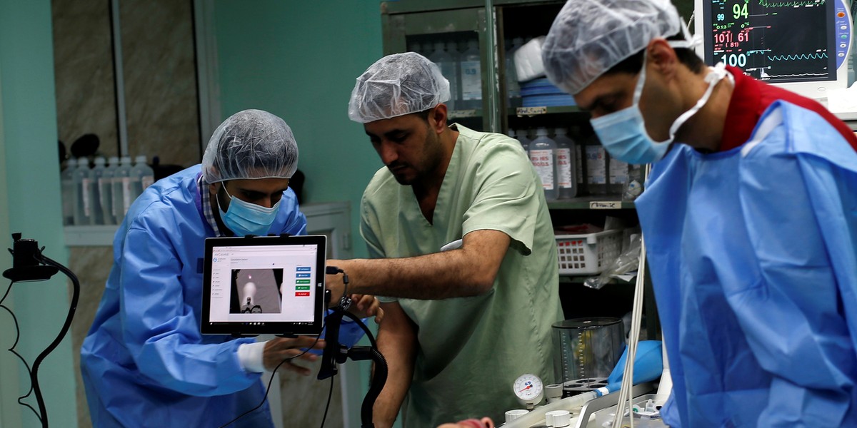 A patient lies on a bed as a technician, left, adjusts a screen before the start of surgery.