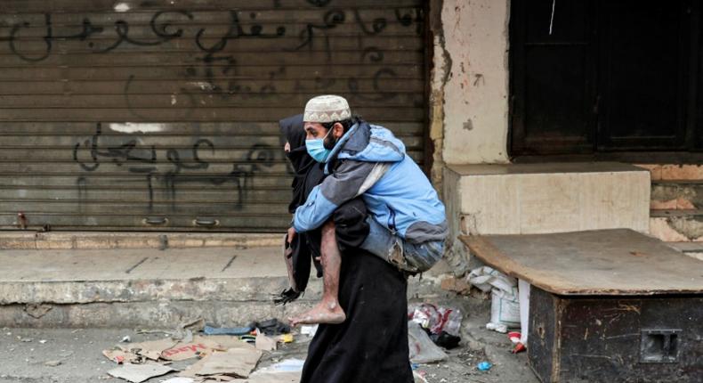 A woman carries a disabled man wearing a protective face mask in the Sabra refugee camp in Lebanon where vulnerable Syrian and Palestinian refugees are bracing for the coronavirus