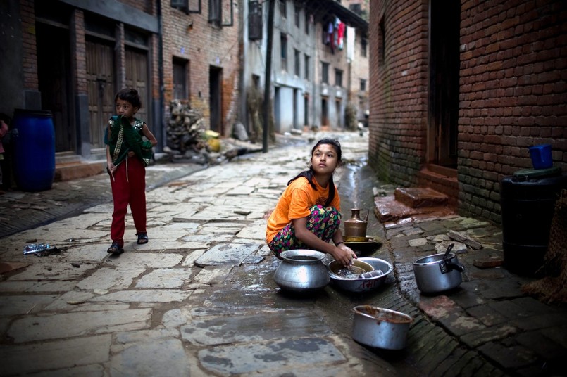 Nepal. Dziewczynka myje naczynia na ulicy osiedla Khokana na przedmieściach Katmandu