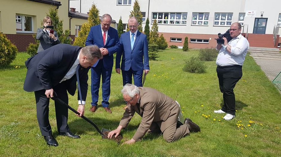 Jarosław Zieliński sadzi drzewo podczas uroczystości w szkole w Raczkach. Klęczy nadleśniczy Wojciech Stankiewicz