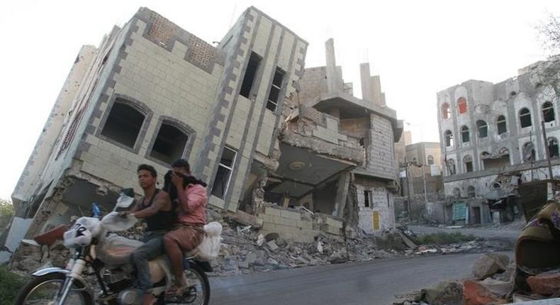 People ride a motorbike past a destroyed house in the southwestern city of Taiz, Yemen