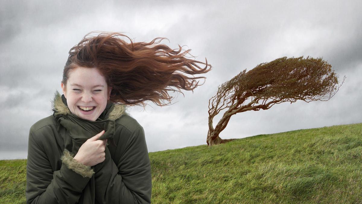 Young woman standing on windswept hill, smiling, eyes closed